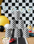 Checkered flag racing party cups stacked in pyramid display - black and white checkered disposable paper cups for race car themed birthday party supplies with racing decorations, balloons, and toy cars for motorsports party celebration