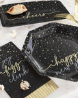 Black paper plates and napkins with gold text on a white surface with popcorn and glasses. Perfect for new year's eve parties