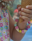 Child wearing handmade ice cream charm bracelet from Cotton Twist beading kit while holding waffle cone - fun summer party craft activity and creative gift for kids jewelry making