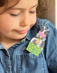 Child wearing a colorful brooch with a cartoon design on a denim shirt.