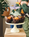 Dinosaur-themed cupcakes on a white cake stand with decorative figures.