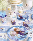 Frozen 2 winter birthday party supplies featuring Anna Elsa Olaf plates, cups, napkins, white layered cake and snowflake decorations for Disney princess theme party