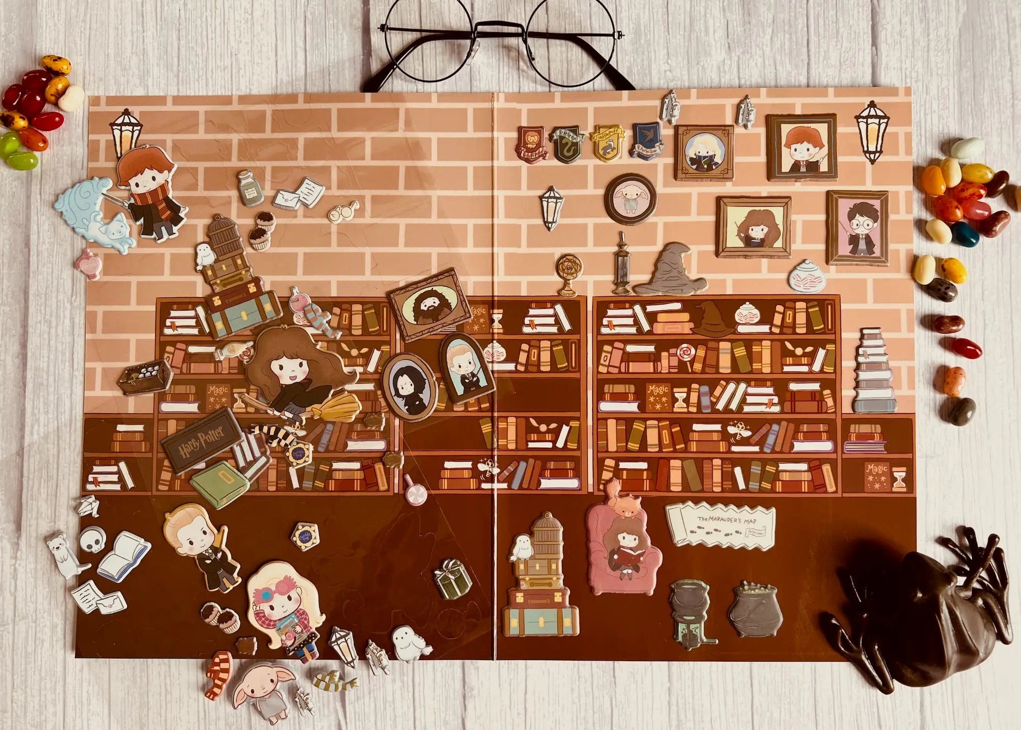 A flat lay of the Hogwarts Puffy Sticker Playset featuring cartoon characters and magical items as puffy stickers on a library background, surrounded by colorful jelly beans, a toy spider, and glasses at the top.