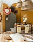 A cozy safari-themed birthday setup featuring a wooden table, neutral cushions, animal print plates, a “wild one” cake, lion accent decor, a gold foil lion balloon, woven lamps, and the Party Lion Fan Set with earth-toned decorations.