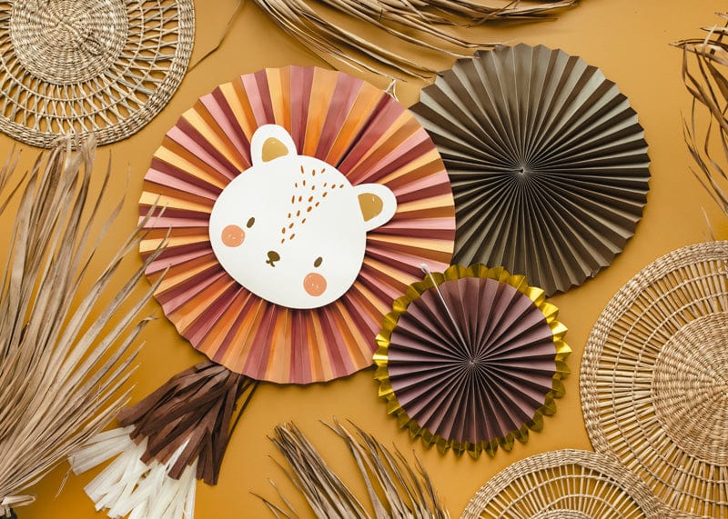 The Party Lion Fan Set features paper fans and woven mats on a mustard yellow surface, with a large striped fan showing a cute bear face, shiny gold foil details, lion head accents, and dried palm leaves among other fan decorations.