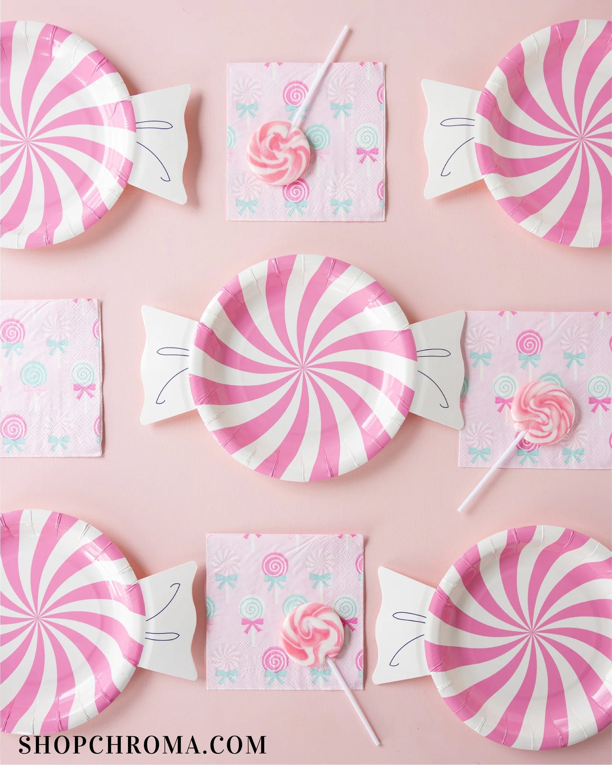 Pink Candy Plates, pink patterned napkins, and pink swirl lollipops create a sweet display on a pastel pink background. From the Candyland Collection. SHOPCHROMA.COM appears in the bottom left corner.