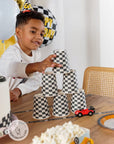 Race car birthday party supplies featuring checkered flag cups and decorations - child playing with racing themed party tableware including black and white checkered paper cups, toy cars, and racing party decorations for kids birthday party
