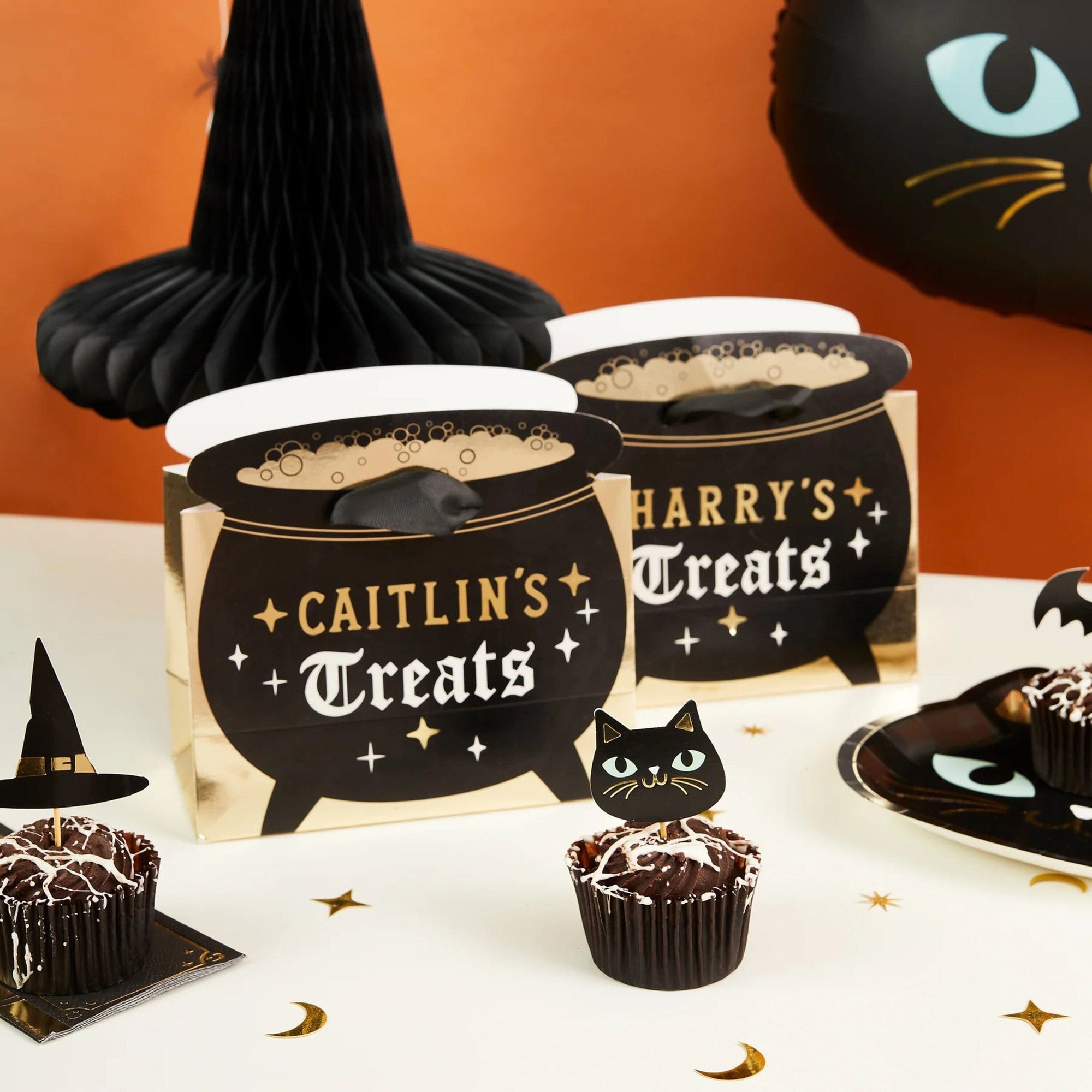 Custom Halloween cauldron favour bags display with personalized names, witch hat decorations, chocolate cupcakes, and spooky party supplies for Halloween birthday parties and themed celebrations