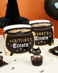 Custom Halloween cauldron favour bags display with personalized names, witch hat decorations, chocolate cupcakes, and spooky party supplies for Halloween birthday parties and themed celebrations