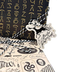 Harry Potter Dark Arts Gift Wrap Set featuring black wrapping paper with gold foil spell symbols - Lumos, Alohomora, Expelliarmus - layered with cream Defense Against the Dark Arts wrapping paper and a die-cut Expecto Patronum stag patronus gift tag tied with black and white baker's twine; ideal for Harry Potter birthday party gifts and Wizarding World themed celebrations