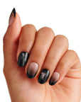 Hand model wearing Kiss x Wicked For Good Elphaba Own Your Power black ombre press-on nails with Elphaba witch hat design; short oval fake nails shown in light