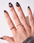 Open hand wearing Kiss x Wicked For Good black ombre and Elphaba witch hat press-on nails with gold rings; short oval fake nails 28-piece kit
