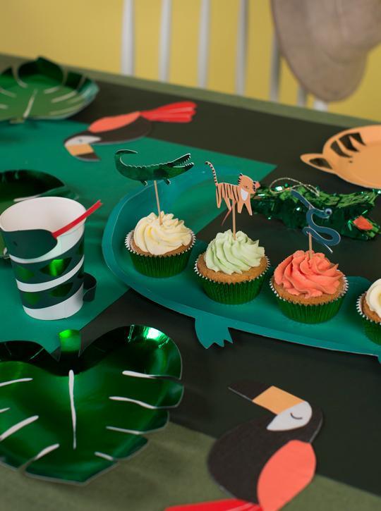 A jungle party table features green leaf plates, bird and animal cutouts, emerald green foil details, frosted cupcakes with animal picks and a 3D paper snake, plus Snake Party Cups—striped cups with red straws from a set of 8.