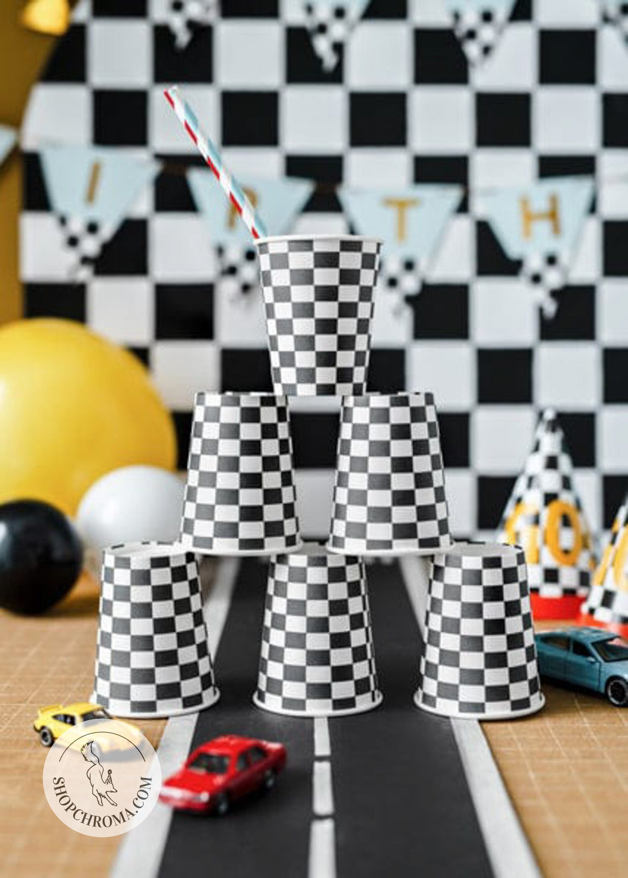 Checkered flag racing party cups stacked in pyramid display - black and white checkered disposable paper cups for race car themed birthday party supplies with racing decorations, balloons, and toy cars for motorsports party celebration