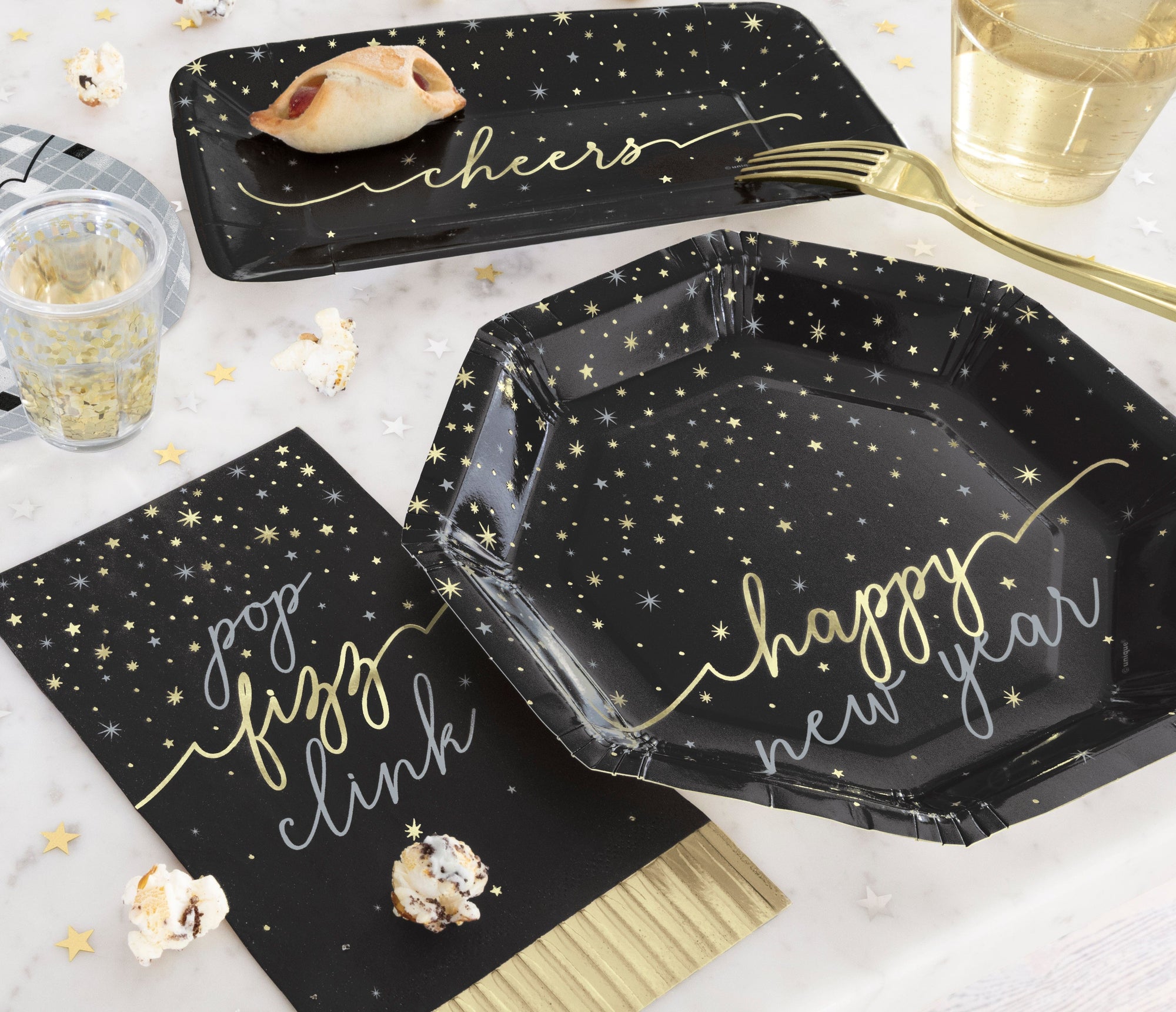 Black paper plates and napkins with gold text on a white surface with popcorn and glasses.  Perfect for new year's eve parties