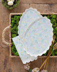 Set of floral-patterned easter themed plates and napkins on a wooden surface with greenery.
