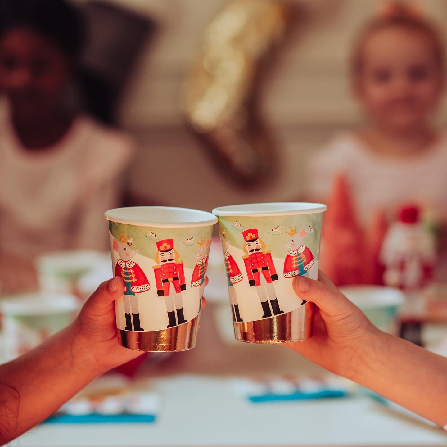 Two hands holding Nutcracker-themed paper cups with a blurred festive background.