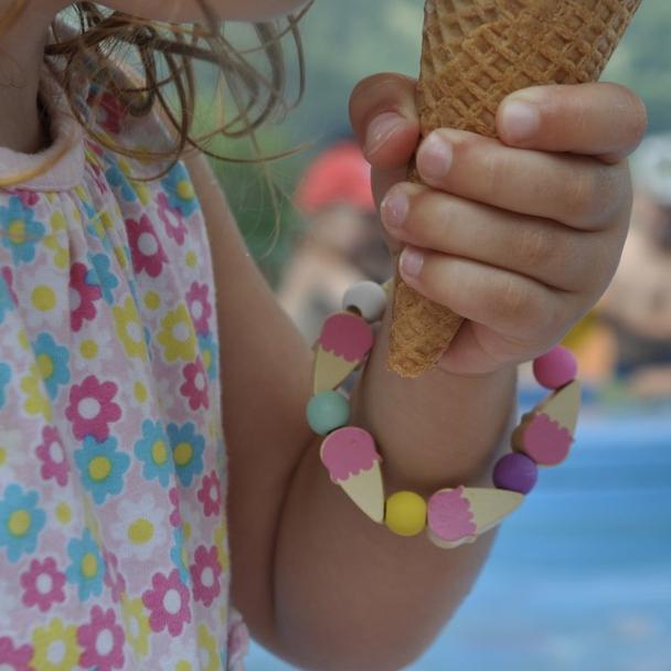 Child wearing handmade ice cream charm bracelet from Cotton Twist beading kit while holding waffle cone - fun summer party craft activity and creative gift for kids jewelry making