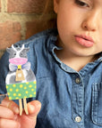 Child holding a paper cow with a bow tie against a brick wall background