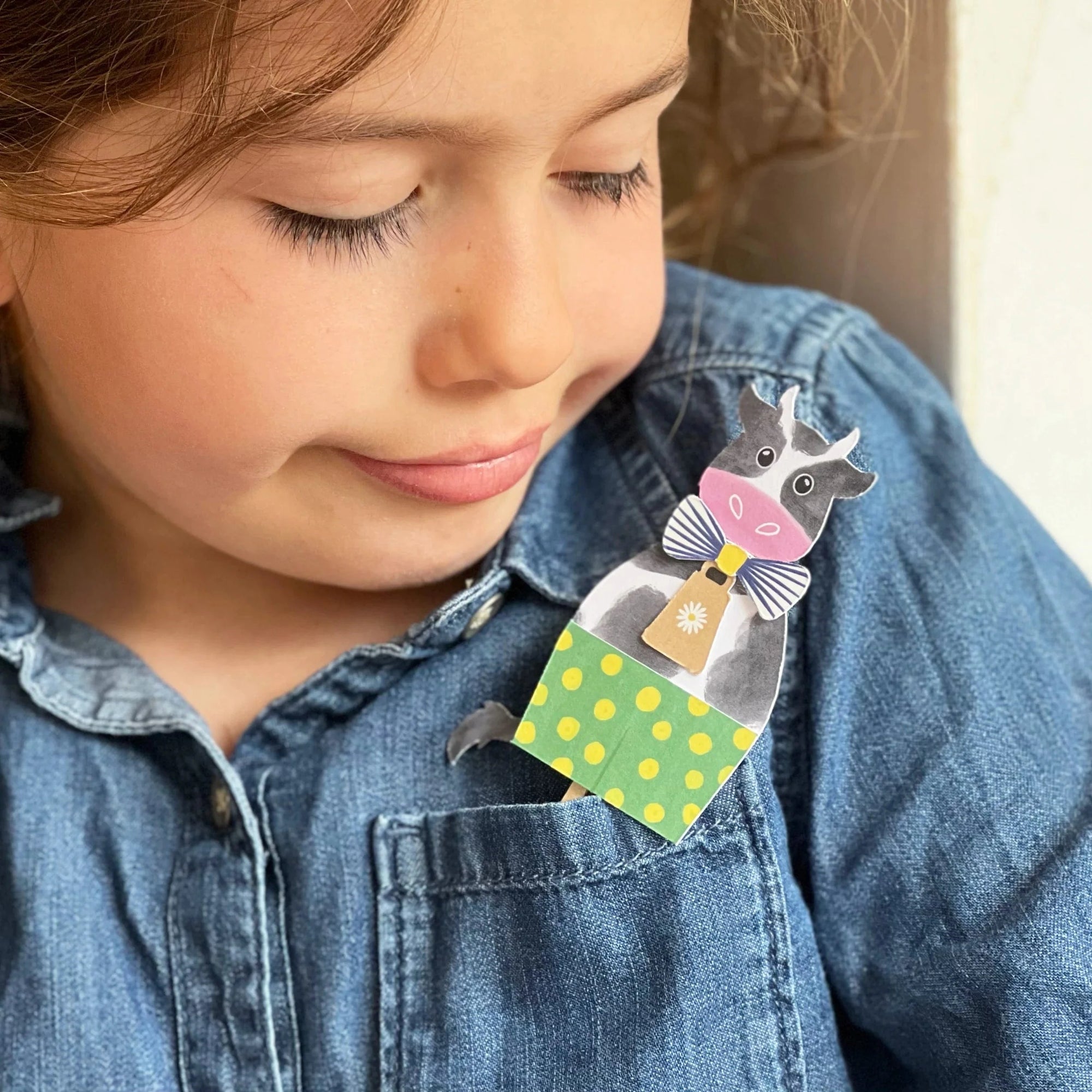 Child wearing a colorful brooch with a cartoon design on a denim shirt.