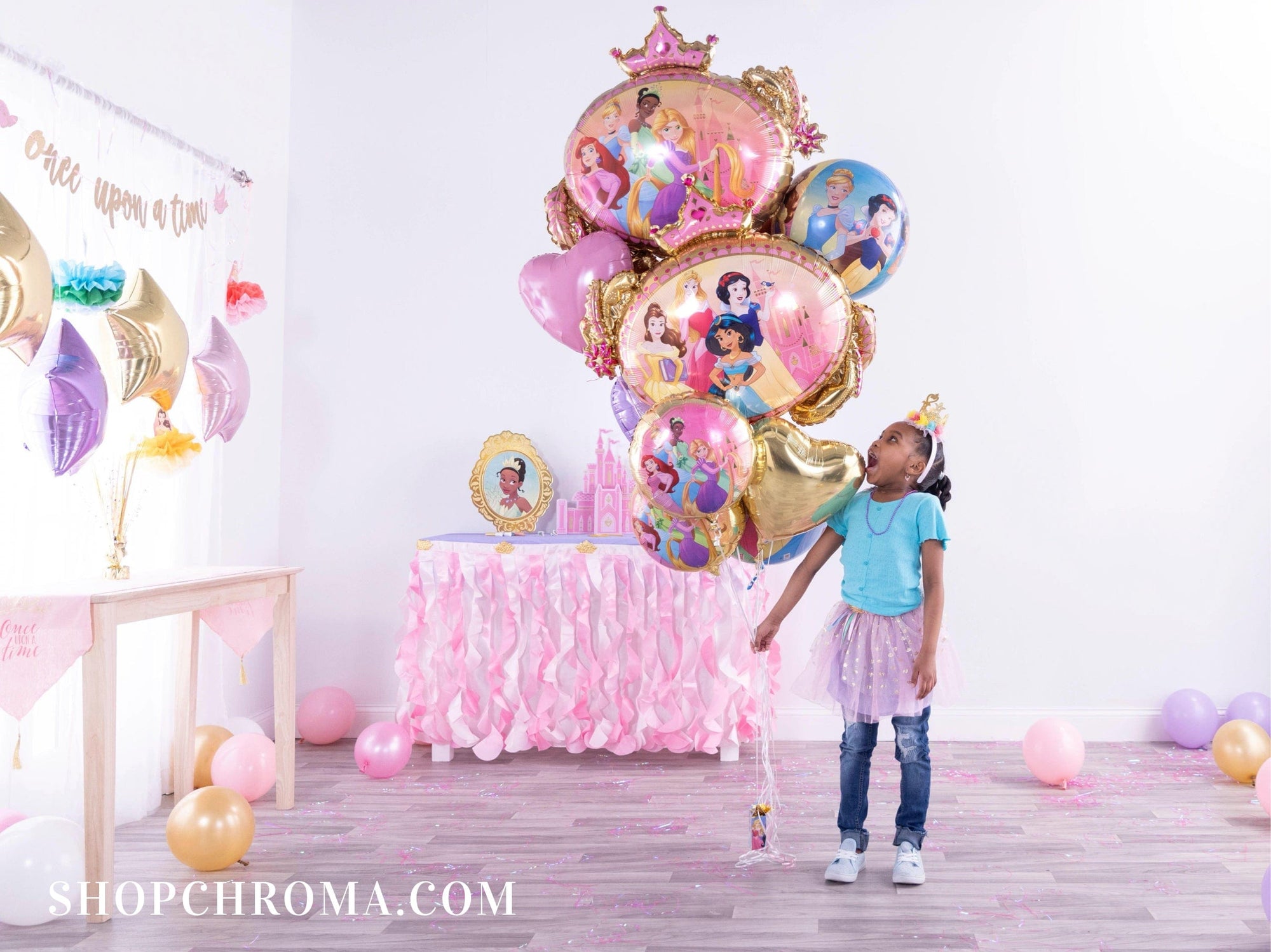 Girl in princess crown holding giant Disney Princess foil balloon bouquet at Once Upon A Time birthday party with pink decor