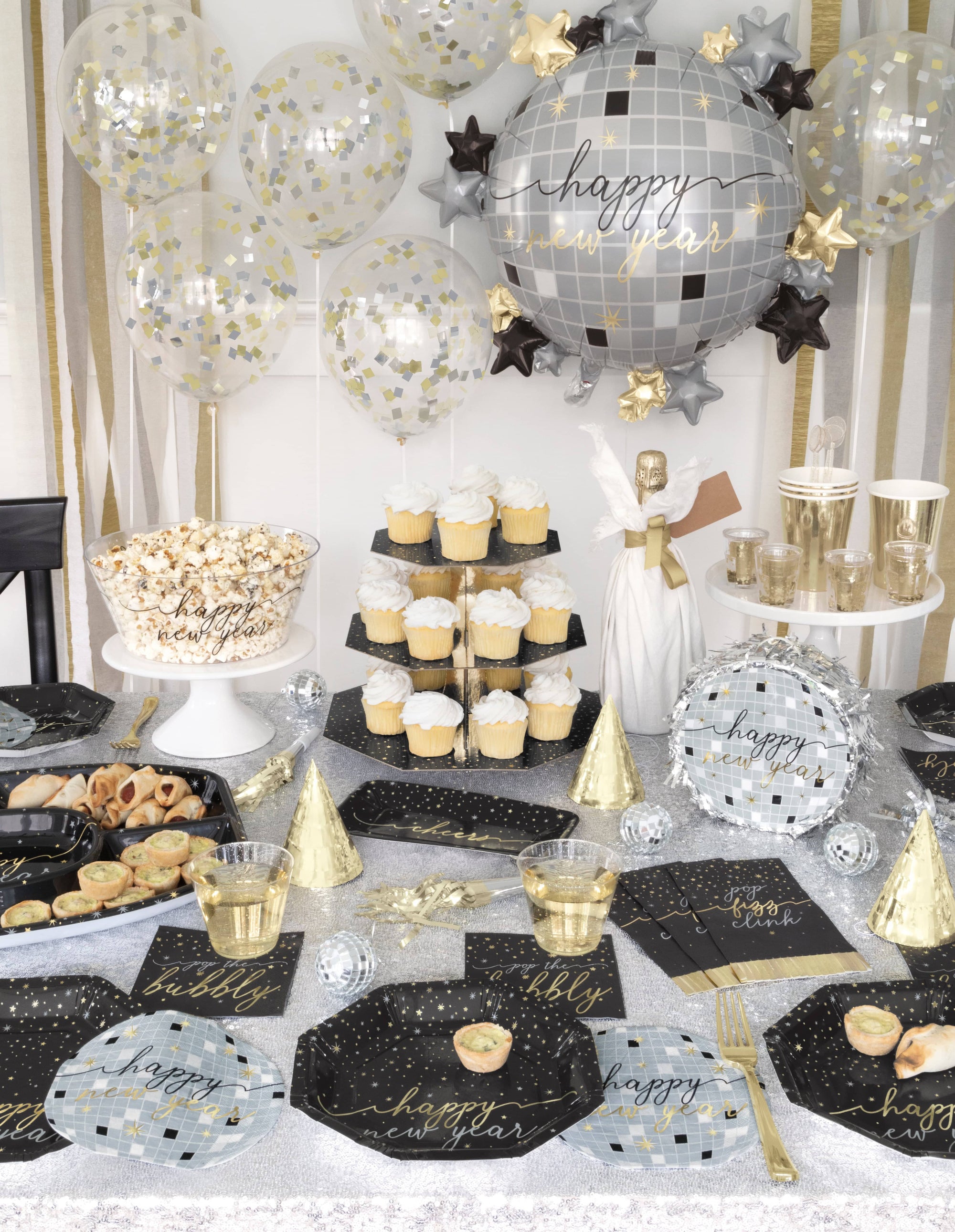Decorated party table with New Year's Eve theme featuring balloons, plates, and dessert stands.