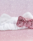 Hello Kitty plush spa and makeup headband with a pink sequin Hello Kitty bow on a glittery pink background