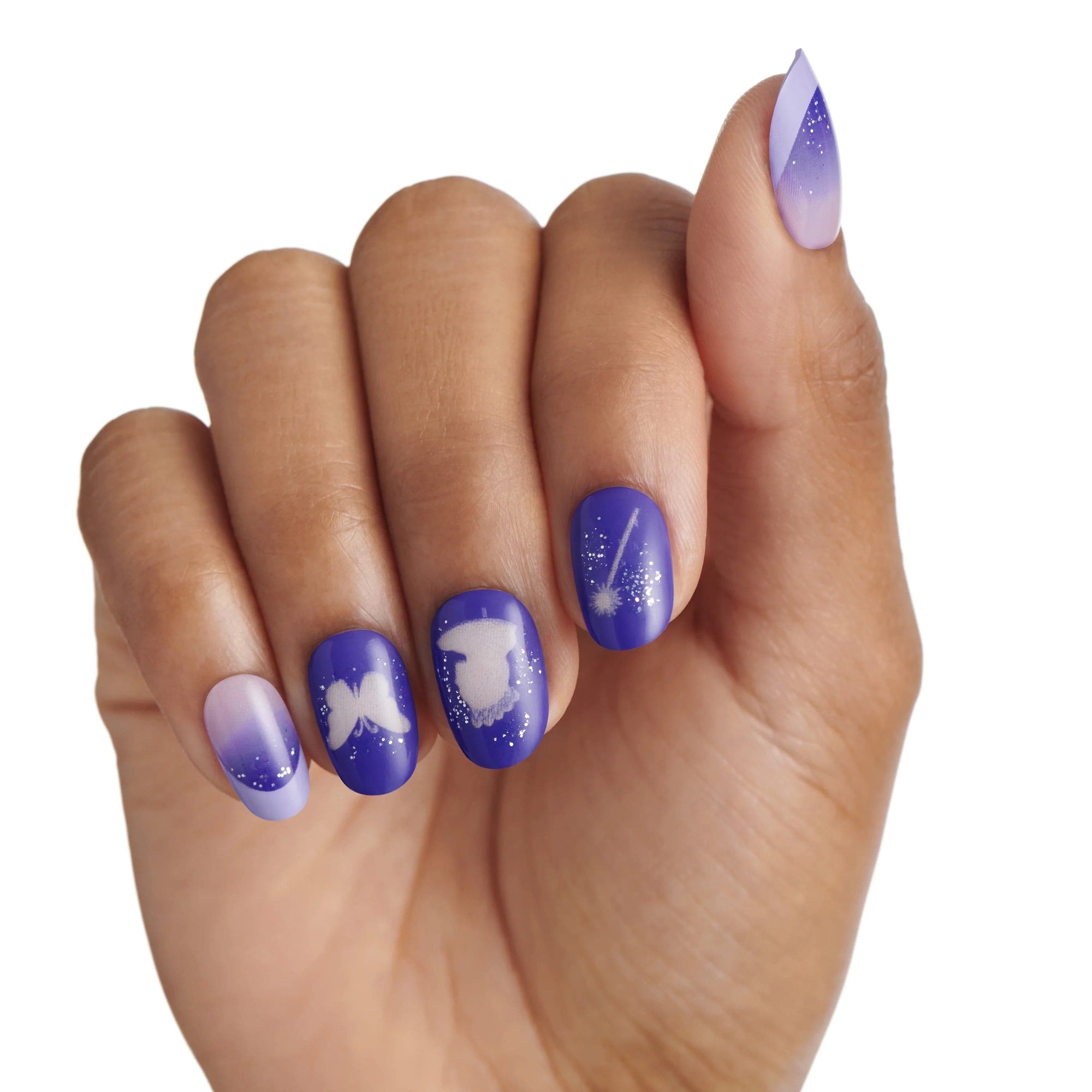 KISS x Wicked For Good Glow With Glinda limited edition press-on nails worn on a hand in natural light, showing purple nails with white butterfly, Glinda silhouette, magic wand designs, and lavender ombre accent nails with glitter