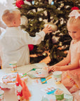 Children decorating a Christmas tree with ornaments and playing with toys on a Nutcracker decorated table.