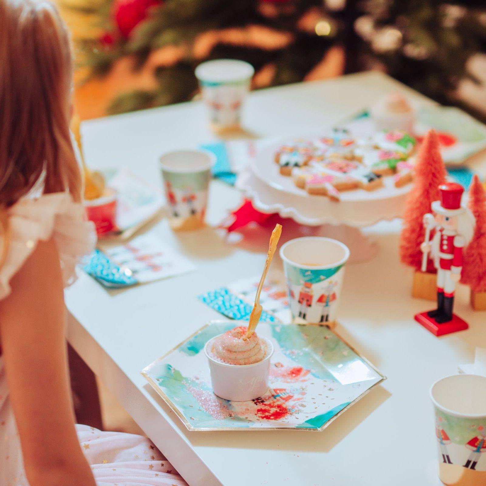 Children's Nutcracker themed table setting with cups, cookies, and a Christmas tree in the background