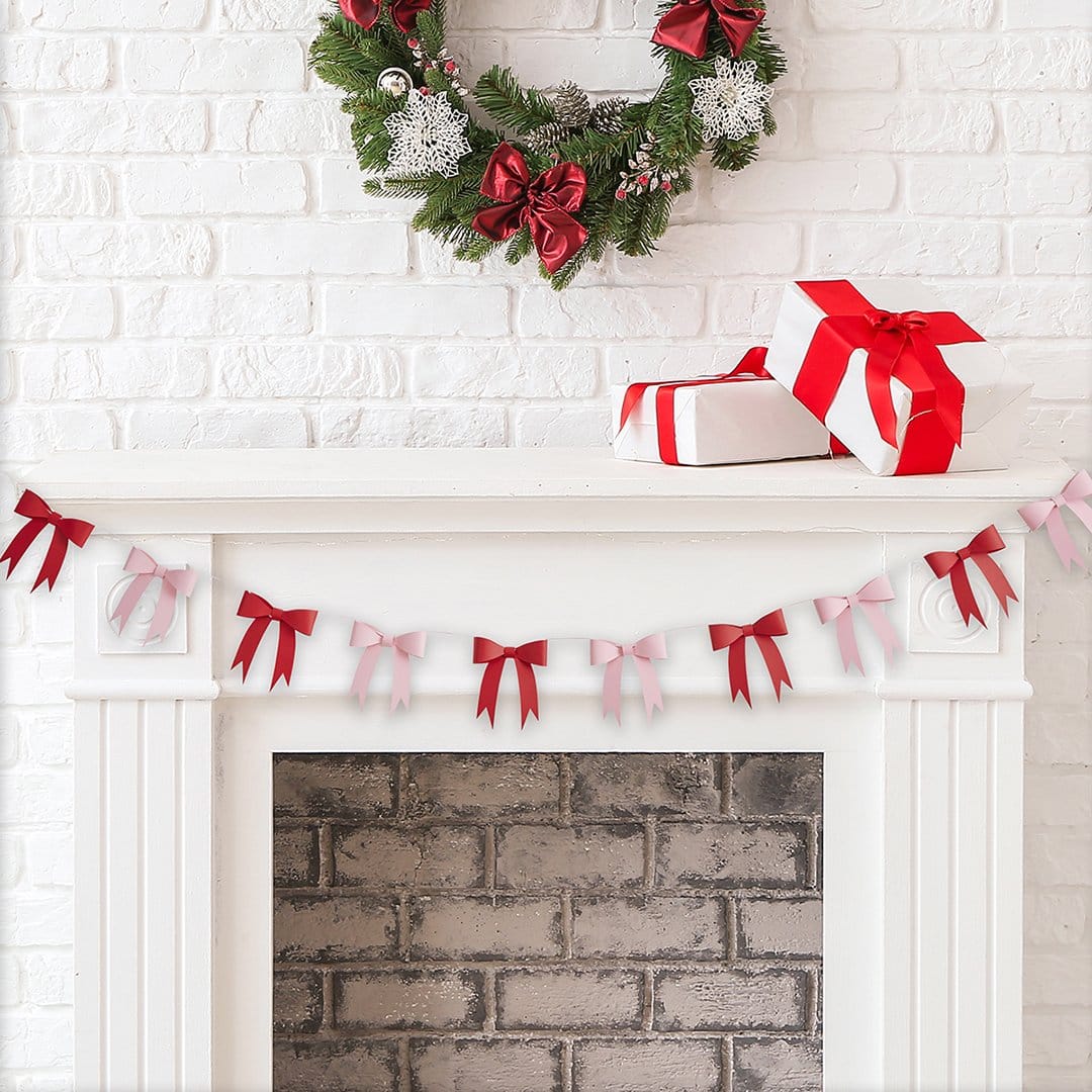Decorative Christmas mantel with wreath, presents, and a pink and red ribbon banner on a white brick wall.