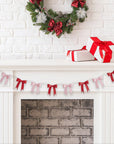 Decorative Christmas mantel with wreath, presents, and a pink and red ribbon banner on a white brick wall.