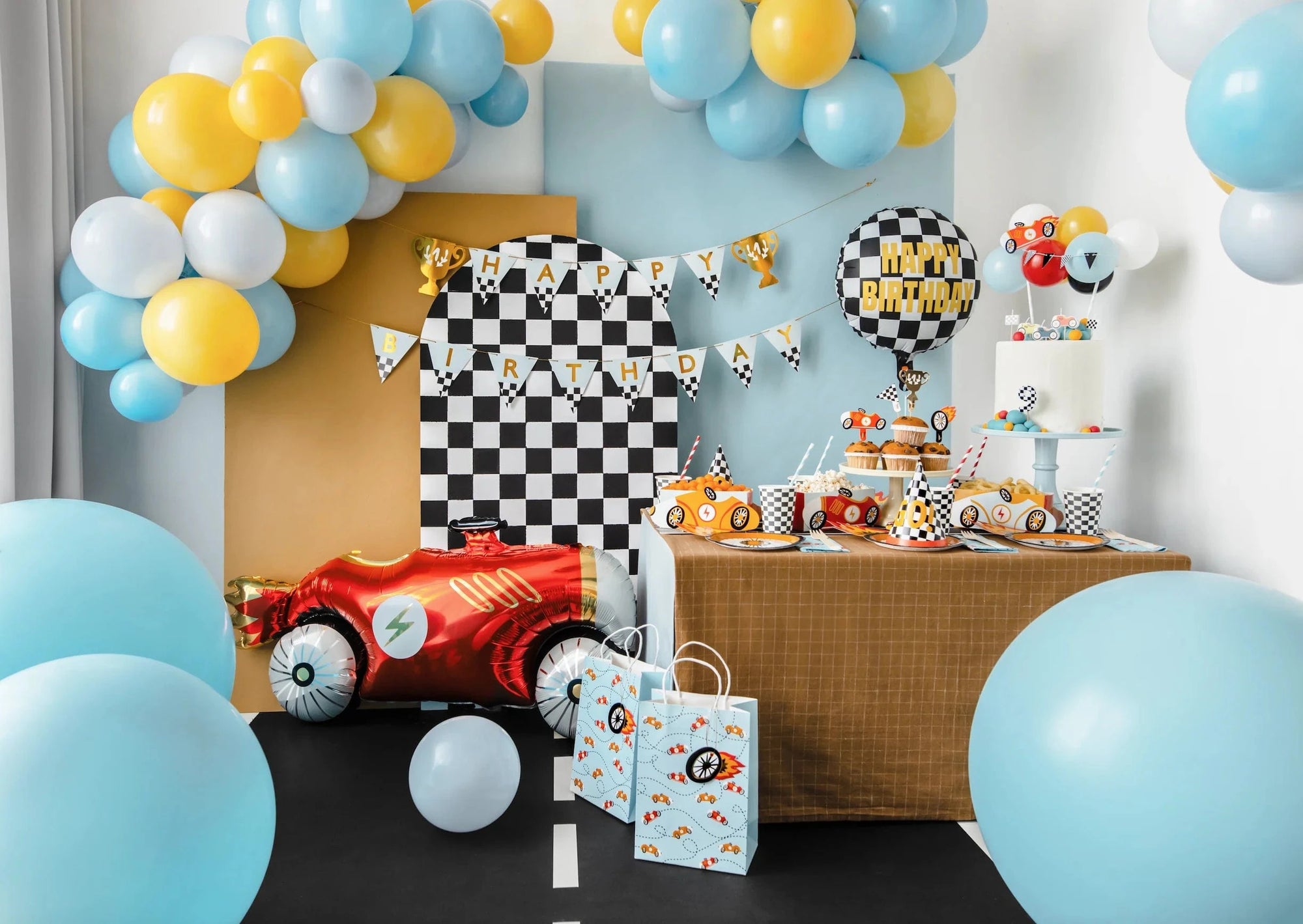 Children's race car themed birthday party setup with balloons, cake, and decorations.