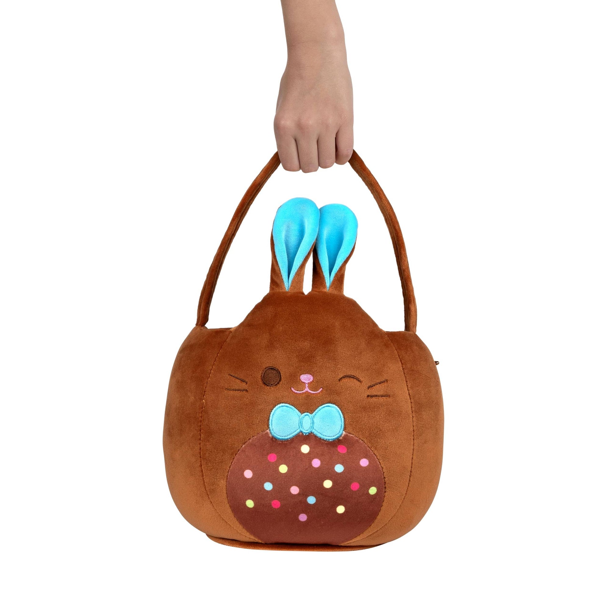 Brown bunny-shaped Squishmallows plush pail with blue ears held by a hand on a white background