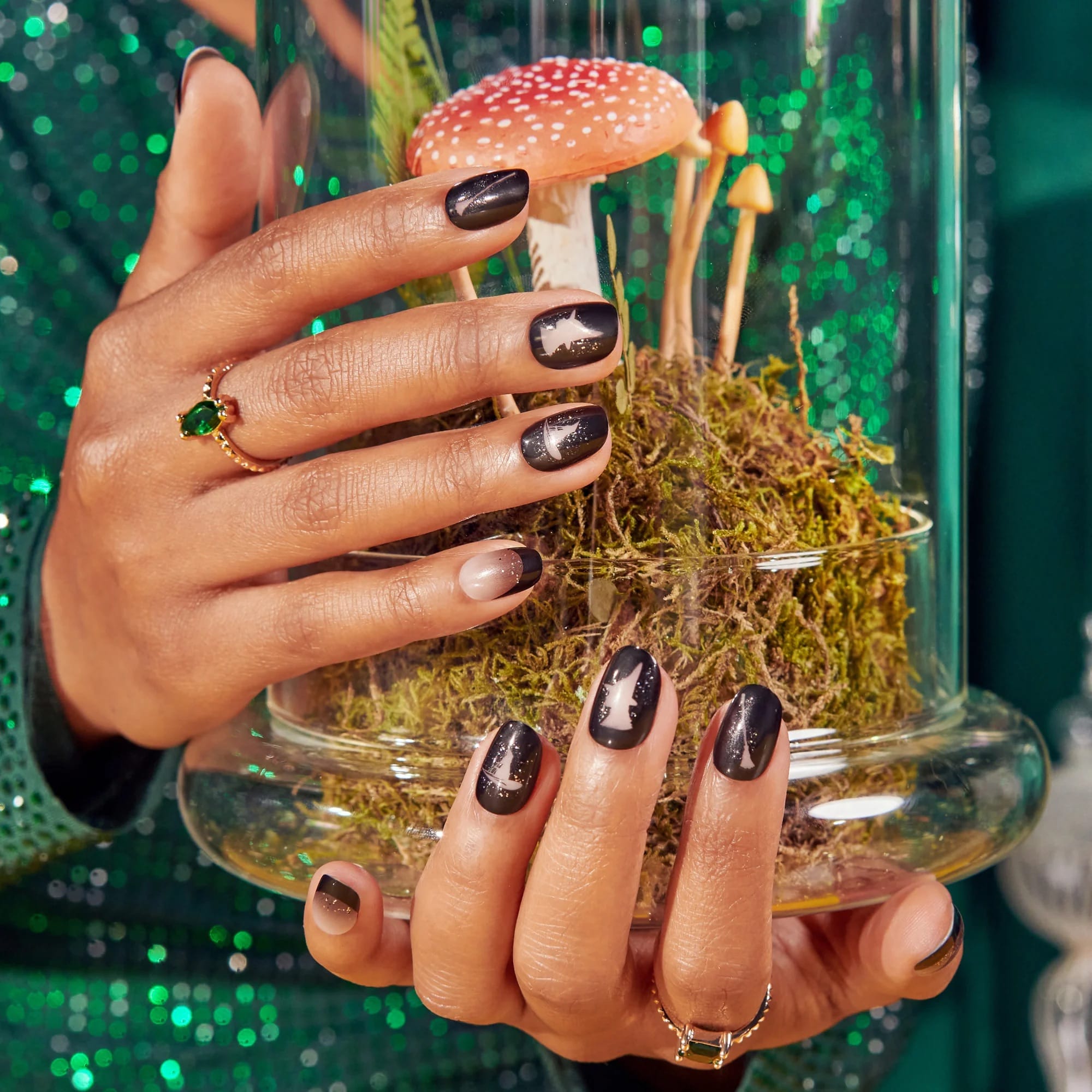 Both hands wearing Kiss x Wicked For Good black Elphaba press-on nails holding terrarium; limited edition Wicked For Good nail kit lifestyle