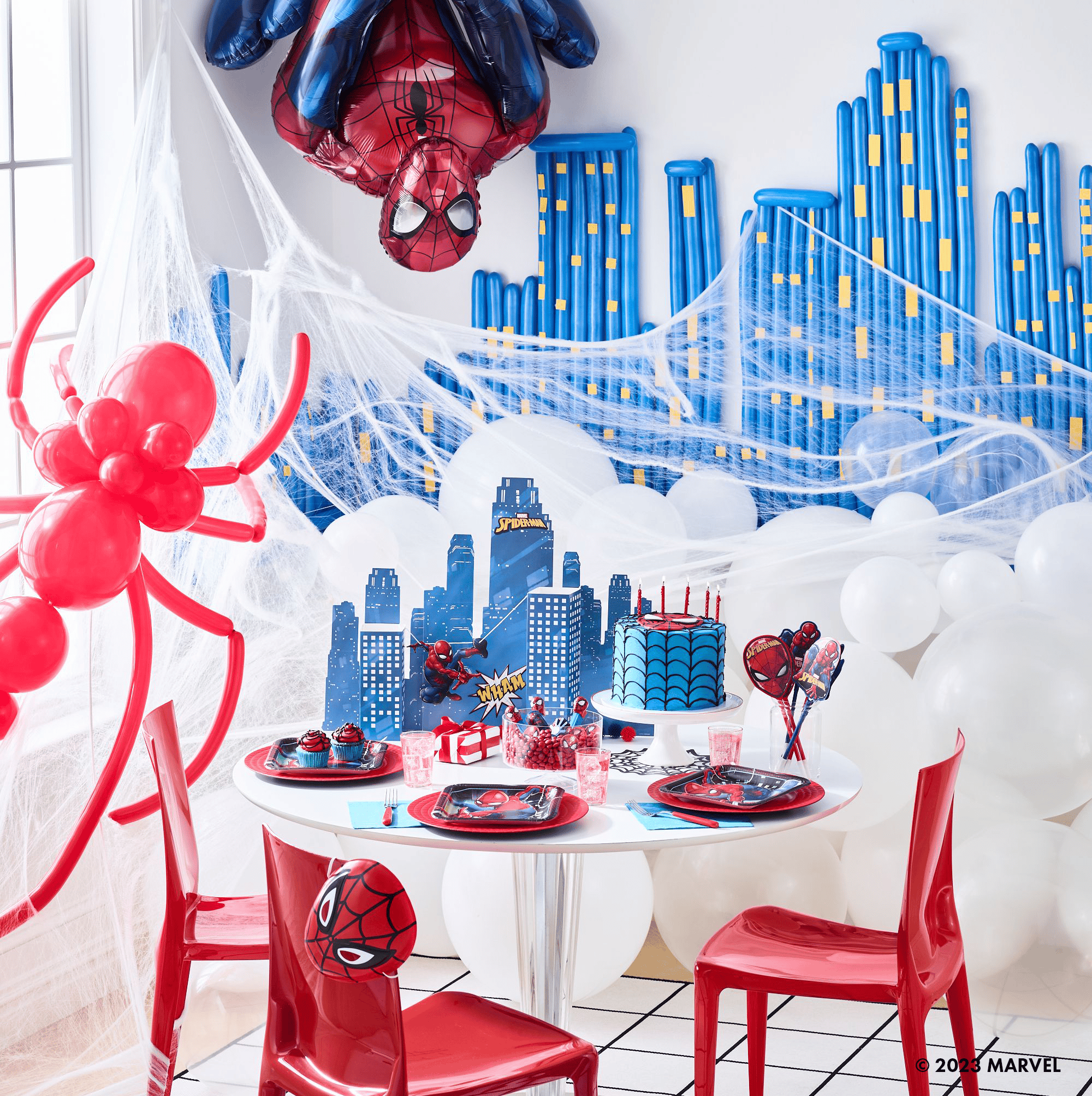 Elegant Spider-Man themed party table setup with NYC city skyline backdrop white balloons themed cake and complete party supplies and decorations for kids birthday