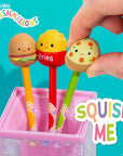 Hand squishing Squishmallows Pep pizza pen topper; Carl, Floyd, and Pep novelty squishy ballpoint pens displayed in pink pencil cup