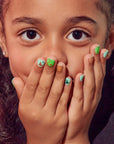 Smiling child covering mouth with hands wearing green and gold Wicked kids press-on nails