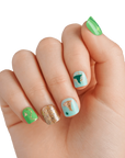Hand wearing Wicked Perfect Duet press-on nails in green, mint blue, and gold glitter with witch hat and moon designs