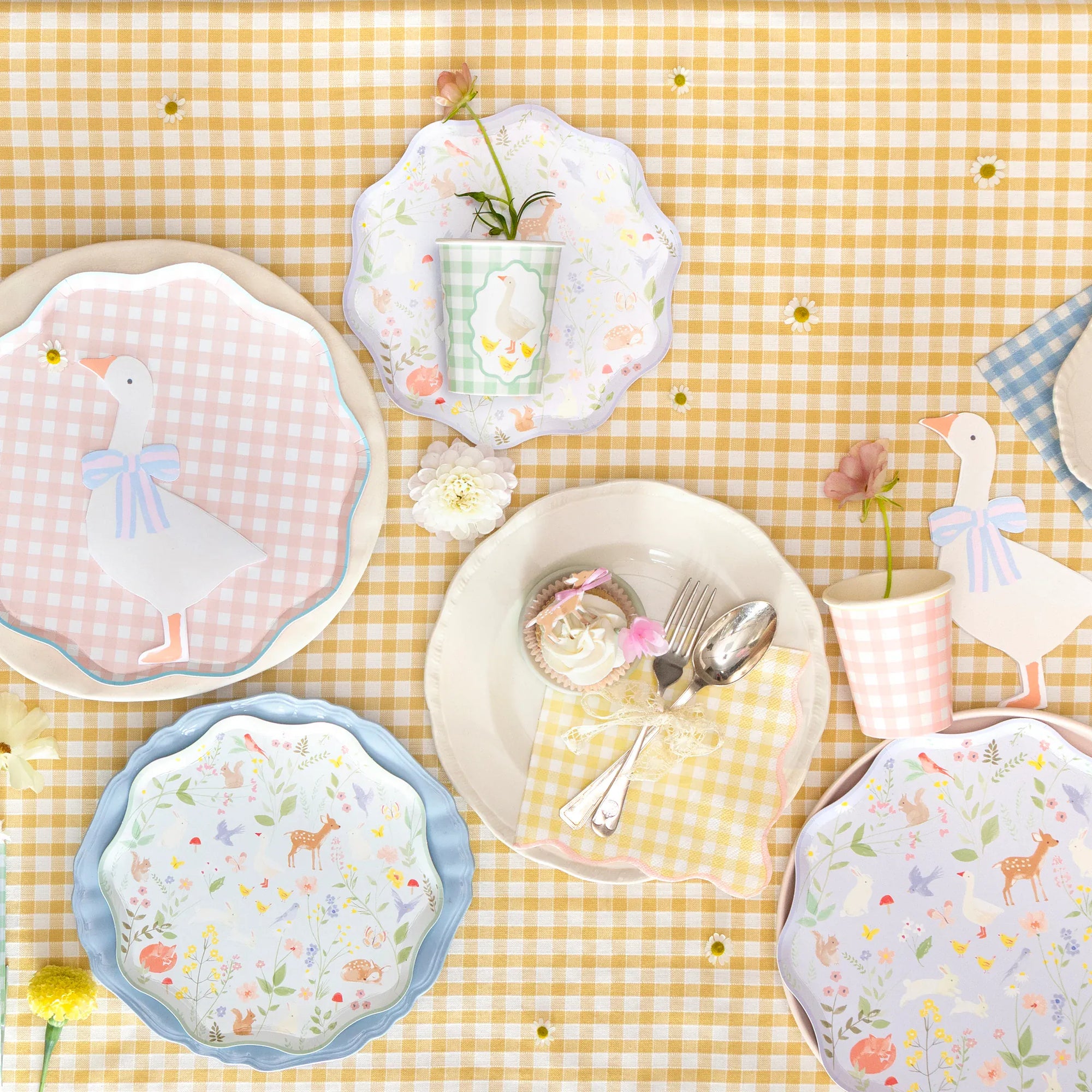 Pastel woodland party table with Little Animals plates, gingham cups and goose place cards on yellow gingham.  Set of decorative plates with animal patterns on a yellow checkered tablecloth.