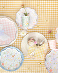Pastel woodland party table with Little Animals plates, gingham cups and goose place cards on yellow gingham.  Set of decorative plates with animal patterns on a yellow checkered tablecloth.