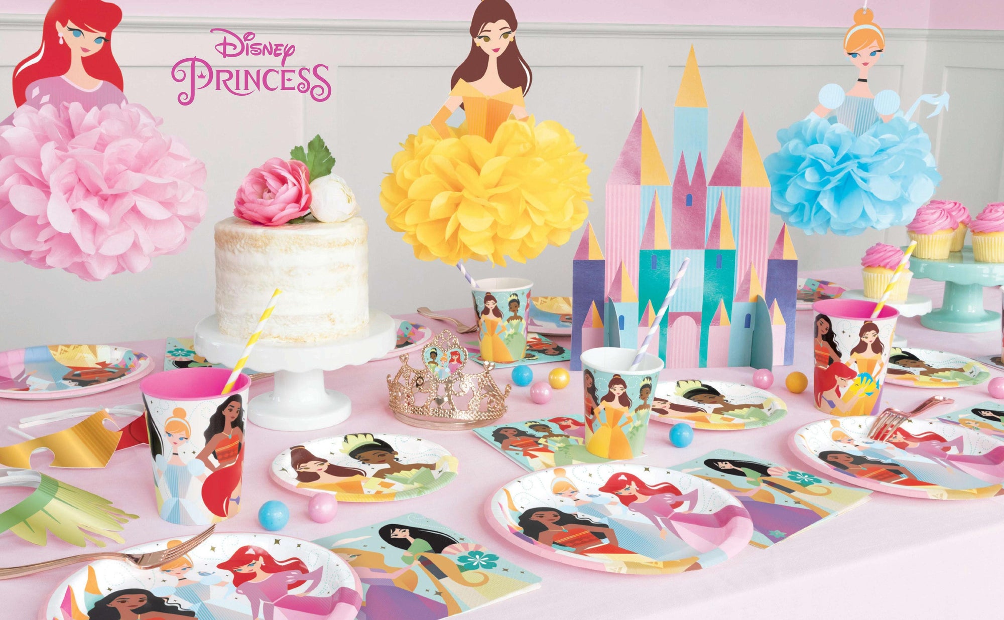 Disney Princess birthday party table setup with hanging pom pom decorations - complete princess themed party supplies tableware and castle centerpiece